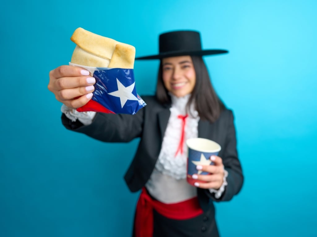 Mujer chilena celebrando Fiestas Patrias con empanada y bebida como parte del aguinaldo de Fiestas Patrias para trabajadores.